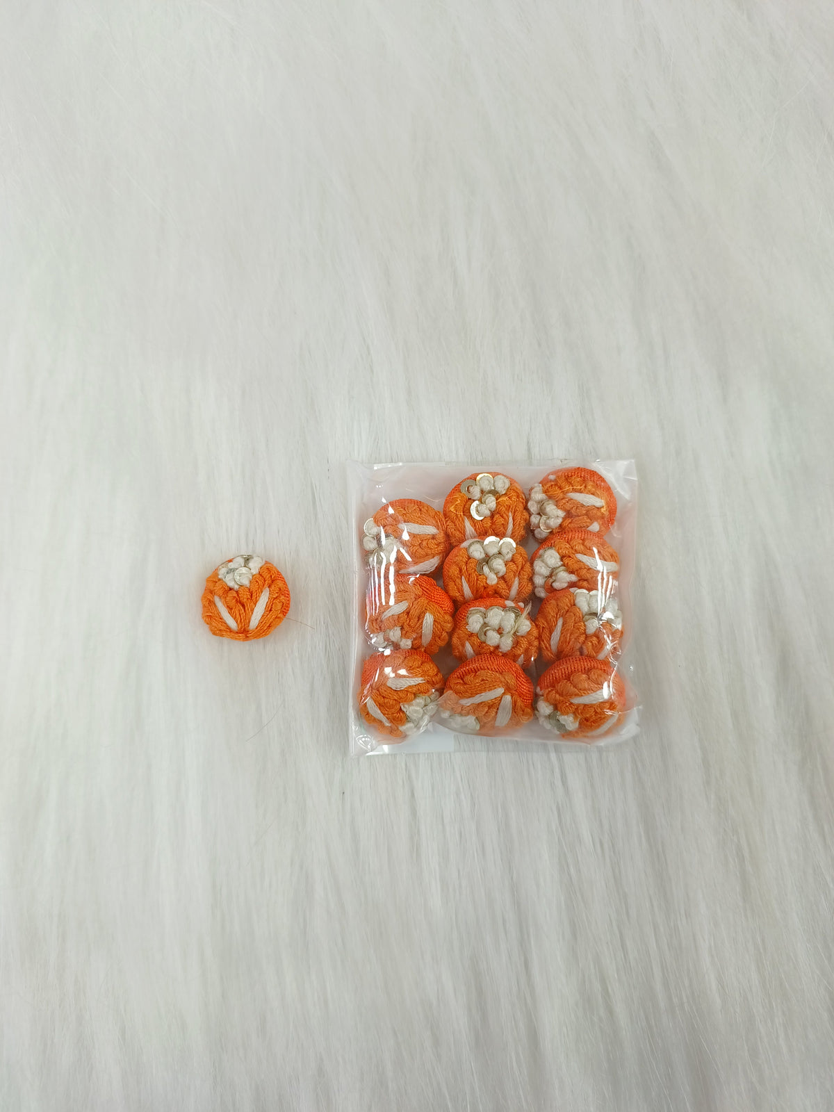 Orange crochet handwork button from Lace Hut with a decorative design, perfect for adding a handmade touch to clothing or crafts.